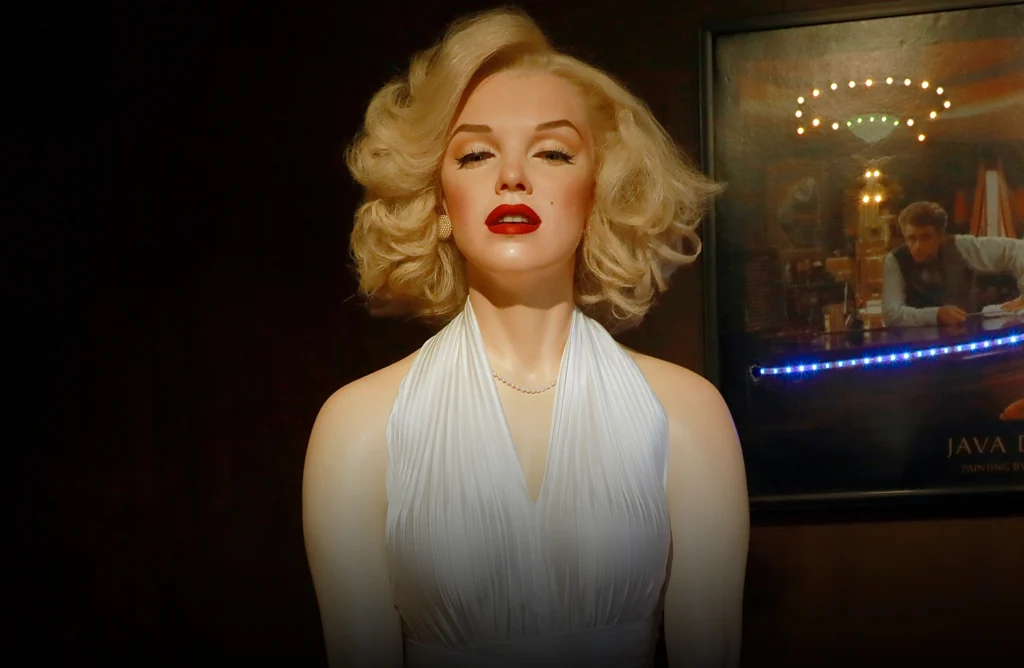 Réplica em cera de uma atriz clássica de Hollywood, com vestido branco elegante, cabelo loiro ondulado e maquiagem marcante, exposta em ambiente temático no Museu de Cera de Gramado.