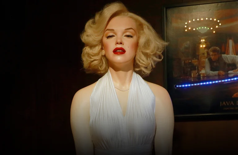 Réplica em cera de uma atriz clássica de Hollywood, com vestido branco elegante, cabelo loiro ondulado e maquiagem marcante, exposta em ambiente temático no Museu de Cera de Gramado.