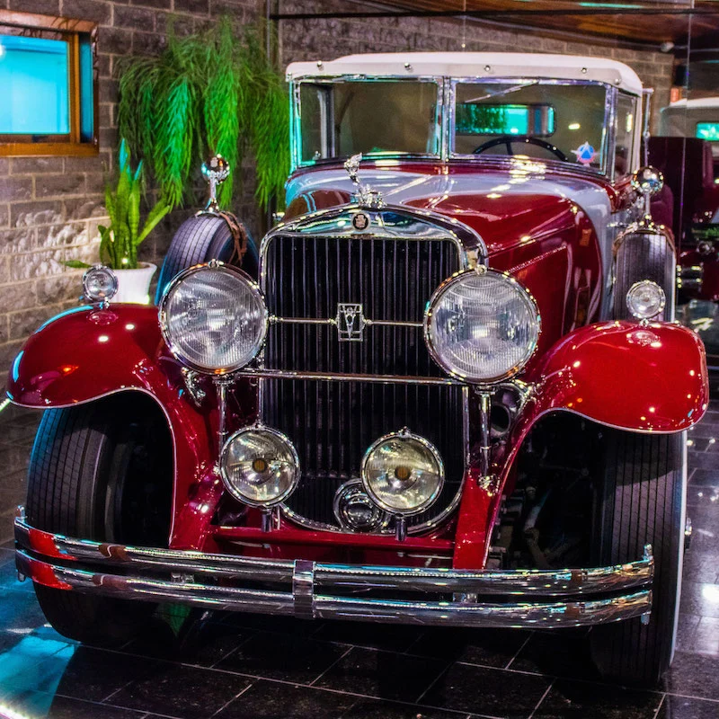 Automóvel clássico da era de ouro do cinema, com pintura vermelha e detalhes cromados, exposto em ambiente interno temático no parque Hollywood Dream Cars, em Canela.