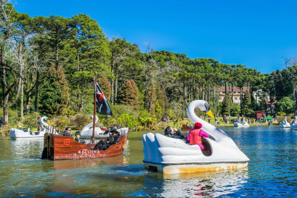 Visitantes aproveitam passeios de pedalinho em formato de cisne e barco pirata no Lago Negro, rodeado por araucárias e áreas verdes, ilustrando a diversão ao ar livre nos parques em Gramado e Canela.