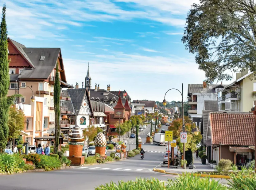 Vista da rua principal de Gramado, com arquitetura europeia, lojas charmosas, árvores e decoração colorida. A imagem ilustra o clima acolhedor da cidade, ideal para quem busca saber o que fazer em Gramado em 3 dias, com uma paisagem que reflete o charme e a beleza da cidade.