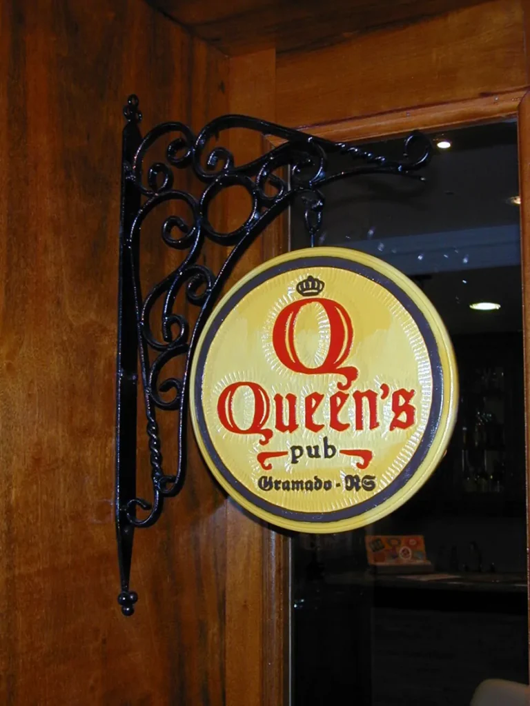 Placa de entrada do Queen's Pub, localizado no Hotel Recanto da Serra em Gramado. A placa, com design clássico, destaca o nome do pub, representando um dos principais bares da cidade, ideal para quem busca aproveitar a vida noturna de Gramado.
