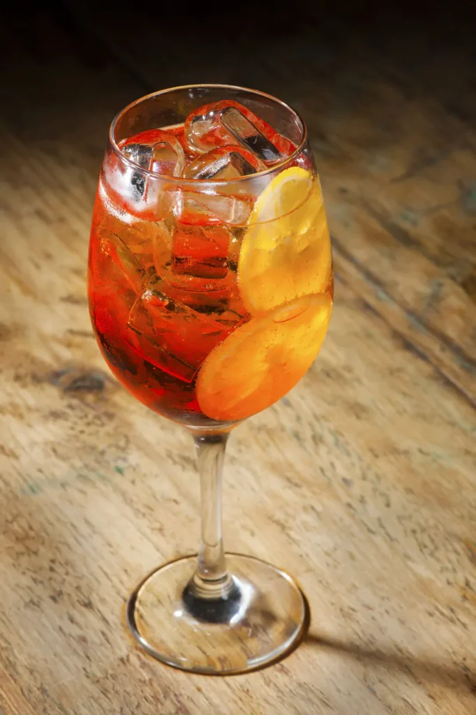 Imagem de um drink refrescante servido no Queen's Pub, localizado no Hotel Recanto da Serra em Gramado. O copo contém uma bebida colorida com fatias de laranja e gelo, representando a variedade e o clima descontraído dos bares em Gramado.
