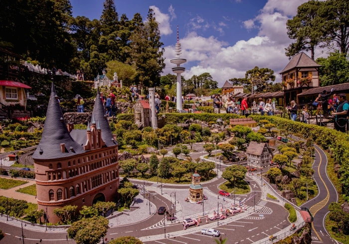 Mini Mundo em Gramado com réplicas detalhadas de construções europeias em miniatura, ruas com carrinhos e jardins bem cuidados, visitantes circulando pelo parque sob céu azul.