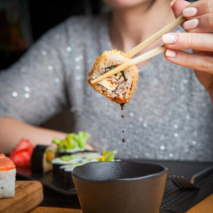 Mulher segurando rolinho de sushi com hashi para representar o sushi em Gramado.