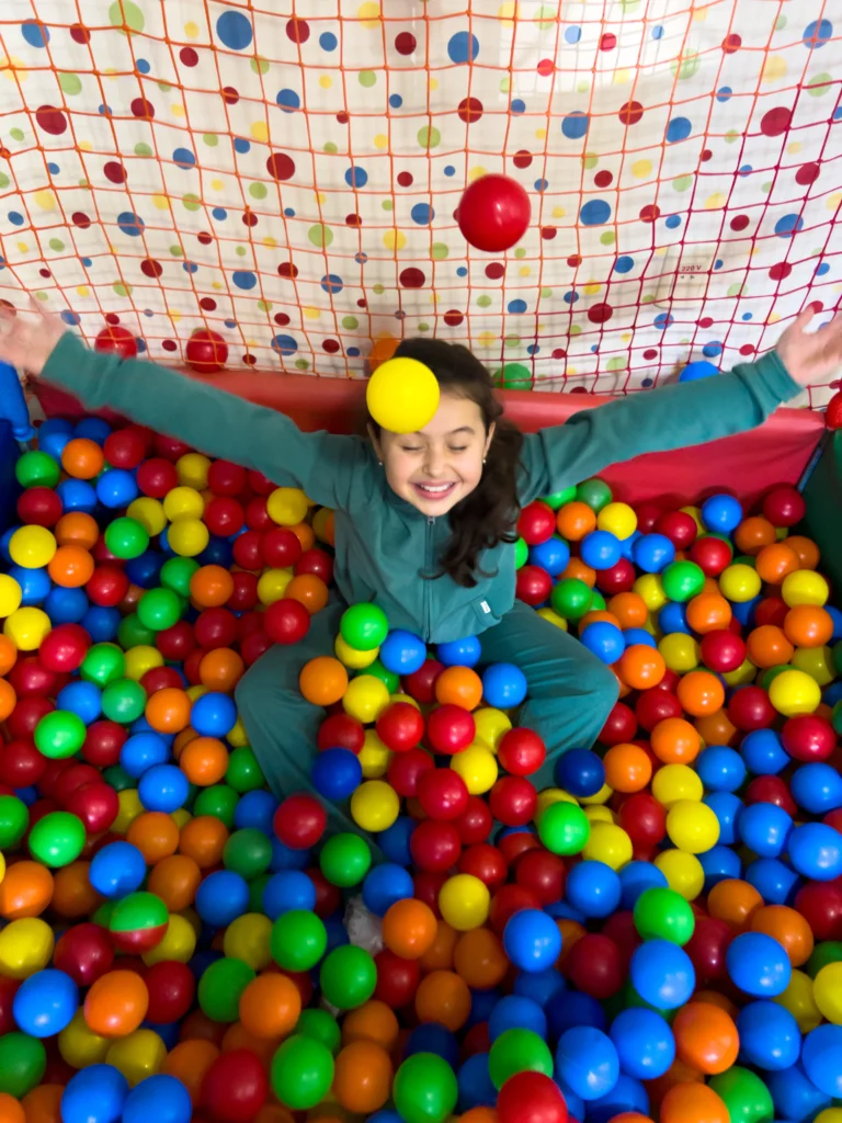 Criança brincando no espaço kids durante as férias de julho no hotel Recanto da Serra, cercada por bolinhas coloridas e se divertindo com alegria.
