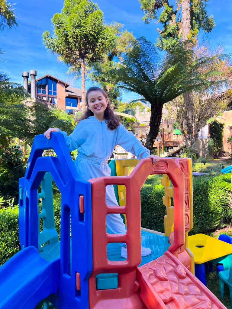 Criança brincando no parquinho ao ar livre durante as férias de julho no hotel Recanto da Serra, aproveitando o dia ensolarado em meio à natureza.