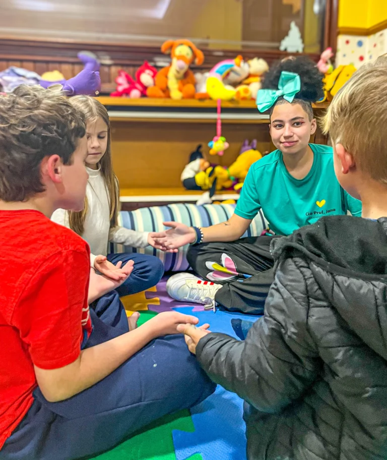 Crianças participando de atividade lúdica com monitora durante as férias de julho no hotel Recanto da Serra, em um espaço interno acolhedor e cheio de brinquedos.
