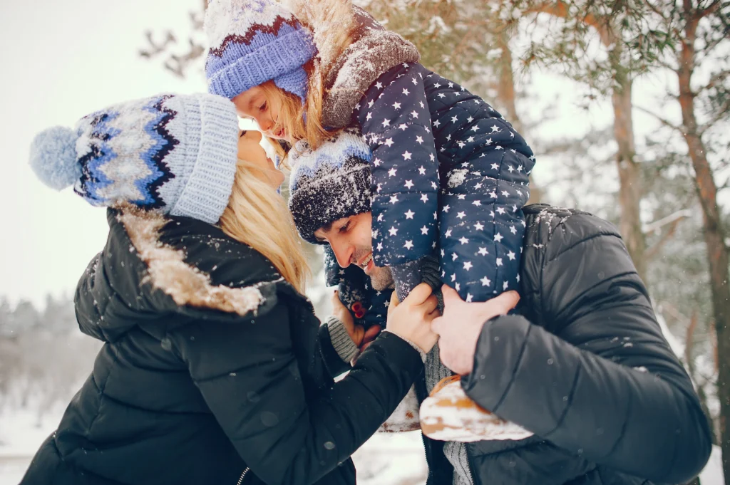Família se divertindo na neve durante o inverno em Gramado em julho, usando roupas de frio em um cenário com árvores e neve ao fundo.