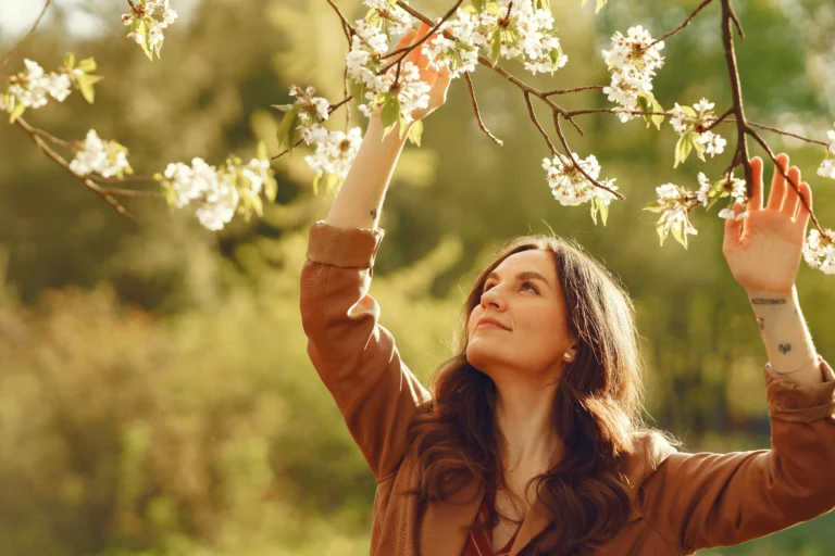 Mulher apreciando flores ao ar livre representando a primavera em Gramado, cercada por natureza e luz suave do sol.