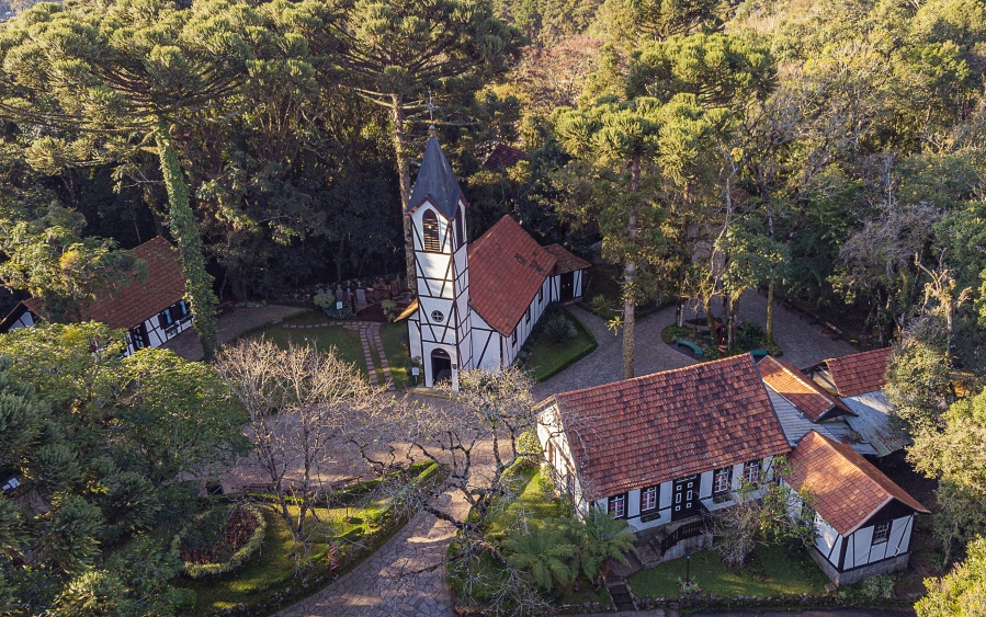 Vista aérea de construções em estilo enxaimel cercadas por araucárias e jardins bem cuidados em meio à natureza, representando o charme europeu típico de Nova Petrópolis, na Serra Gaúcha.
