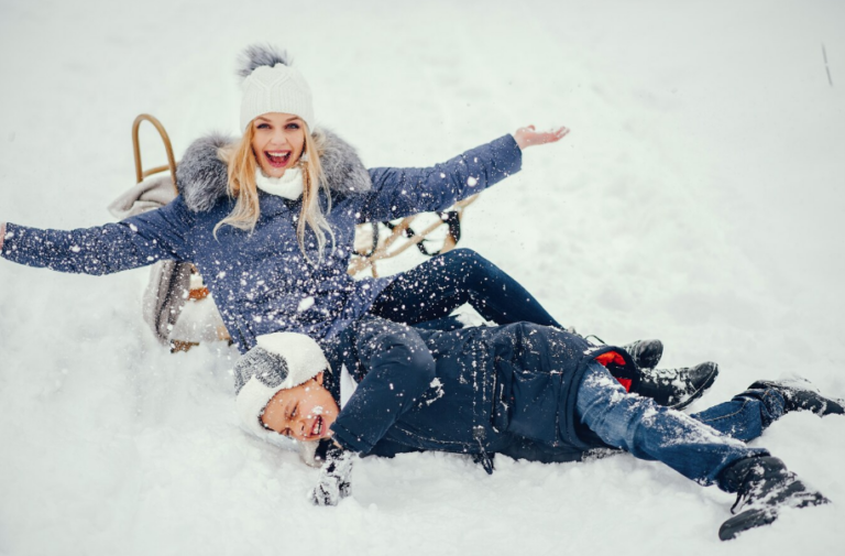 Casal se divertindo na neve com trenó, representando os parques temáticos em Gramado.