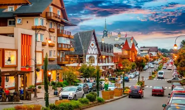 Vista da charmosa avenida central com arquitetura europeia, carros e turistas circulando entre as diversas lojas em Gramado.