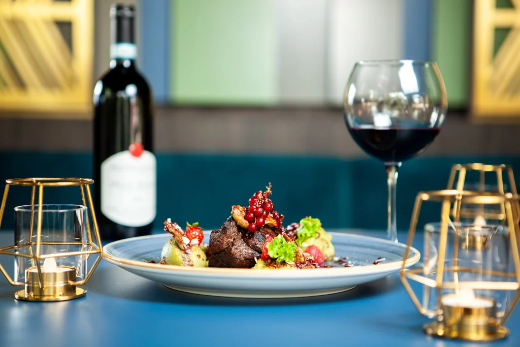 Prato sofisticado com carne, legumes e vinho tinto, em mesa elegante com velas, representando a alta gastronomia dos restaurantes franceses em Gramado.