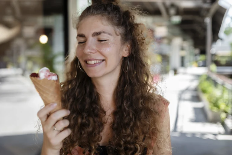 Mulher sorridente segurando casquinha de sorvete colorido em um dia ensolarado, representando a experiência única de visitar uma sorveteria em Gramado.