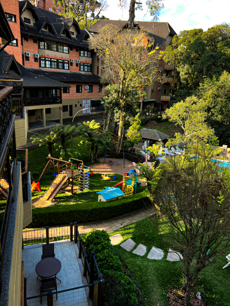 Vista do jardim do Hotel Recanto da Serra, em Gramado, com um playground colorido para crianças e áreas verdes, proporcionando um ambiente ideal para um Carnaval em família na Serra Gaúcha.