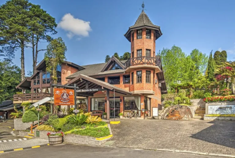 Fachada charmosa do Hotel Recanto da Serra em Gramado, rodeada por jardins floridos e natureza exuberante, refúgio ideal para férias de verão na Serra Gaúcha.