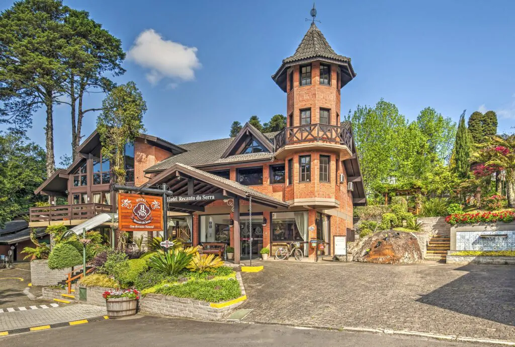 Fachada charmosa do Hotel Recanto da Serra em Gramado, rodeada por jardins floridos e natureza exuberante, refúgio ideal para férias de verão na Serra Gaúcha.