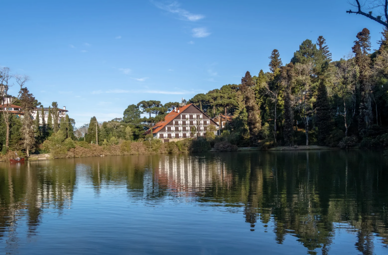 Vista do Lago Negro em um dia ensolarado de verão em Gramado, com água refletindo as árvores, destacando a natureza vibrante da Serra Gaúcha.