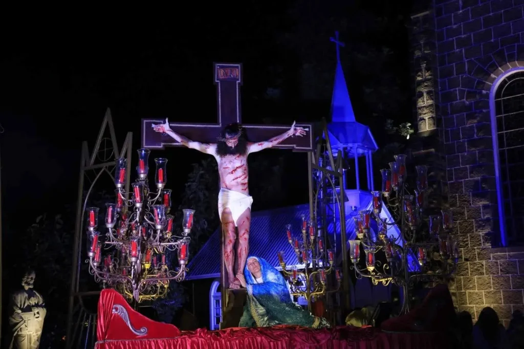 Fiéis participam da Procissão de Ramos em frente à Igreja Matriz São Pedro Apóstolo, em Gramado, marcando a abertura do evento Gramado Aleluia. No centro, encenação religiosa com personagens bíblicos, enquanto o público ao redor acompanha segurando ramos, sob céu, criando um ambiente solene e simbólico da celebração.