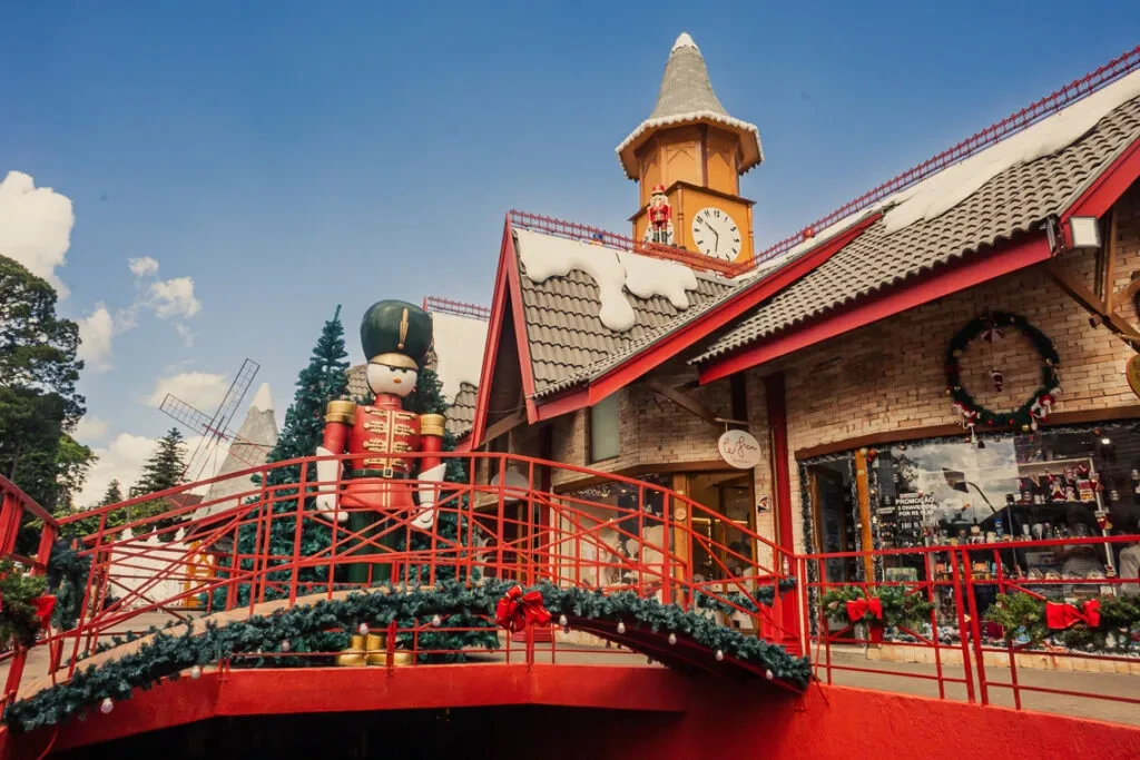 Aldeia do Papai Noel em Gramado no inverno, com ponte decorada e cenário natalino que encanta famílias nas férias de julho.
