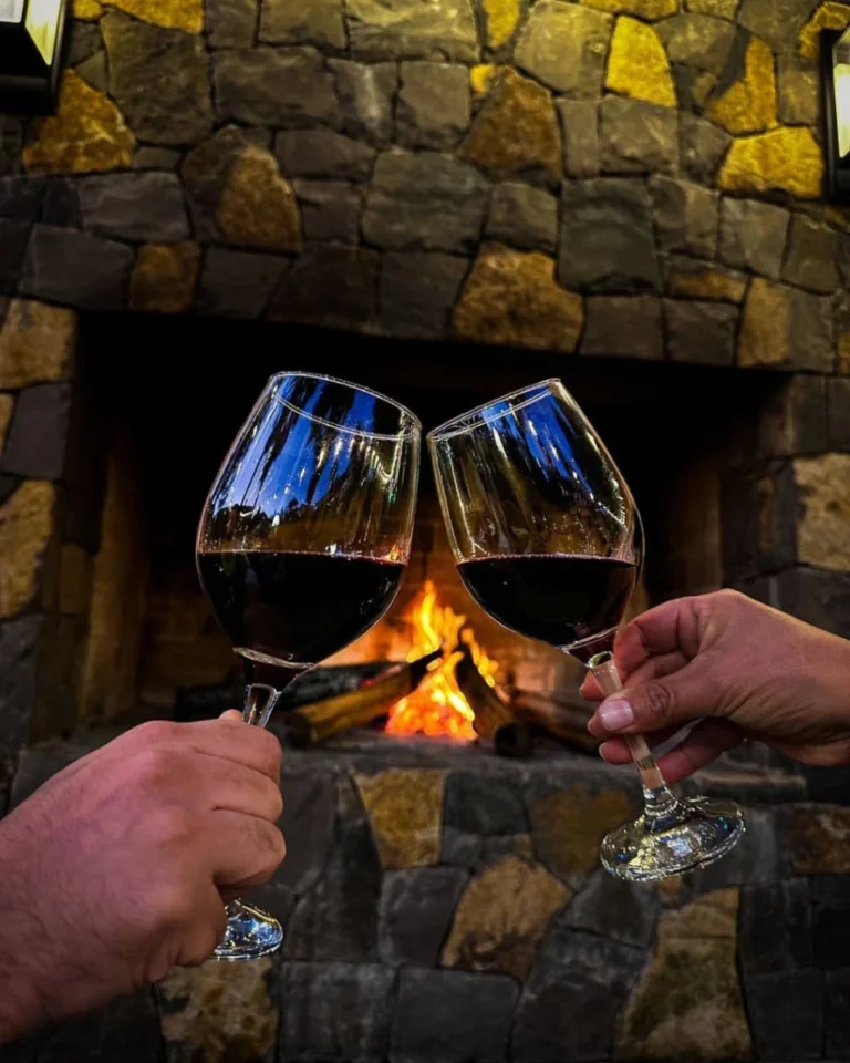 Casal brindando com vinho em frente à lareira no inverno em Gramado, experiência acolhedora na Serra Gaúcha.